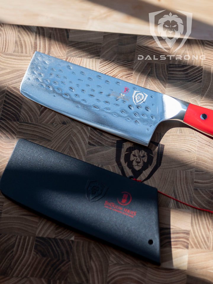 Dalstrong shogun series 6 inch nakiri knife with crimson red handle and black sheath on top of the Dalstrong wooden board.
