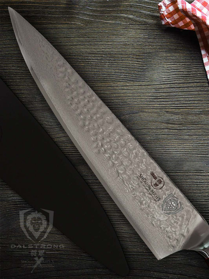Dasltrong shogun series 10.25 inch chef knife with black sheath beside it on a wooden table.