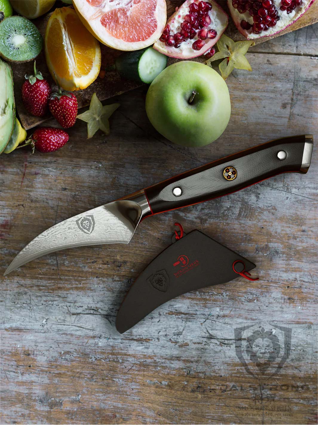Dalstrong shogun series 3 inch bird beak paring knife with black handle and different kinds of fruits on top of it.