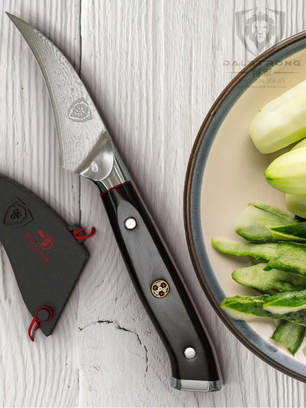 Dalstrong shogun series 3 inch bird beak paring knife with black handle a peeled cucumber on the side.