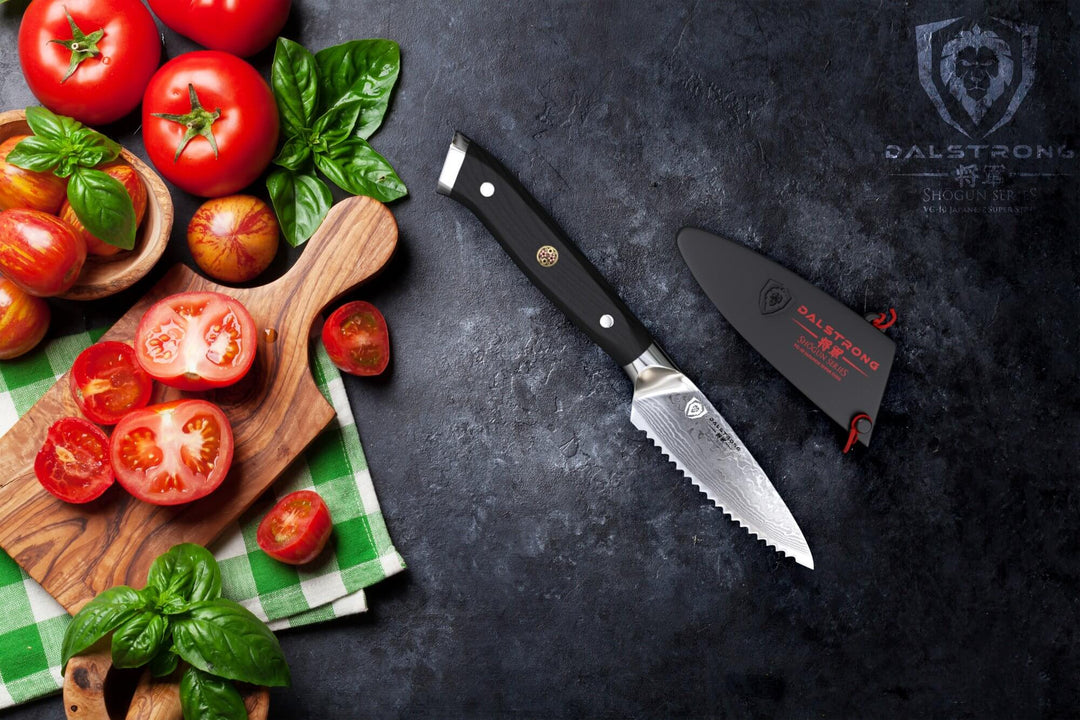 Dalstrong shogun series 3.5 serrated paring knife with black hande and sliced tomato on a wooden board.