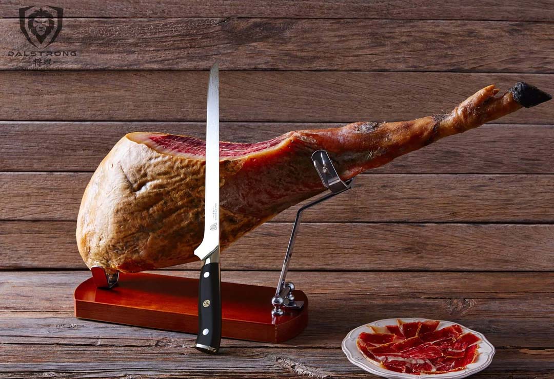 Dalstrong shogun series 12 inch spanish slicer knife with a huge ham leg beside it.