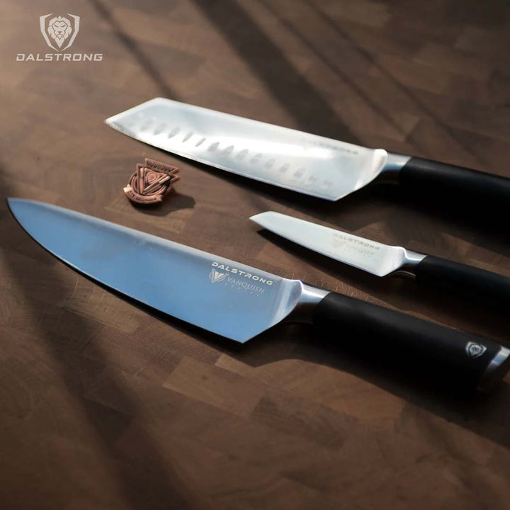 Dalstrong vanquish series 3 piece knife set with black handles and pin on a cutting board.
